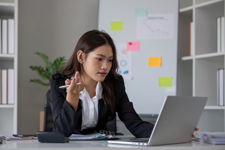 Portrait of young Asian woman working on laptop in modern office Perform accounting analysis, report investment data. Financial concepts and tax systemの写真素材