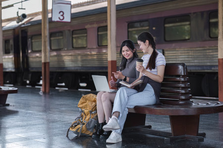 Two Asian female tourist friends are at the train station. Waiting for the train to travel to the provinces together on the weekend.の写真素材