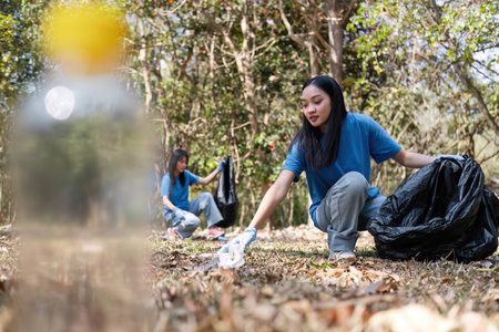 A group of Asian volunteers collects trash in plastic bags and cleaning areas in the forest to...