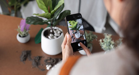 A young Asian woman uses her phone to take photos and enjoys planting plants in her garden to create...