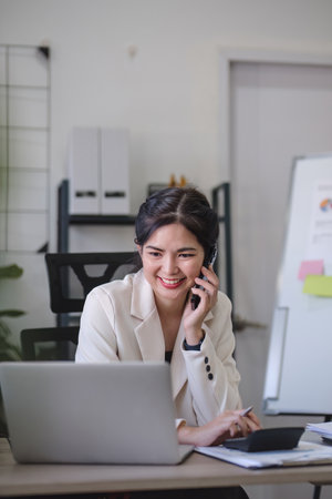 Young Asian business woman sits on the phone in an online business meeting using a laptop in a...