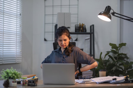 Asian businesswoman feeling tired and stressed over an unsuccessful business while working in a home office decorated with soothing green plants.の写真素材