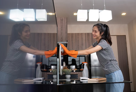 A beautiful young housekeeper wears orange gloves and uses a cloth to clean the table and living room.の写真素材