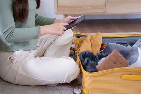 A young Asian female tourist checks off her list. Prepare to pack in your suitcase for traveling on...