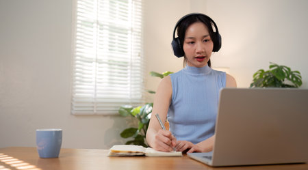 Asian college student sit at home studying online using a video calling program on their laptop.の写真素材