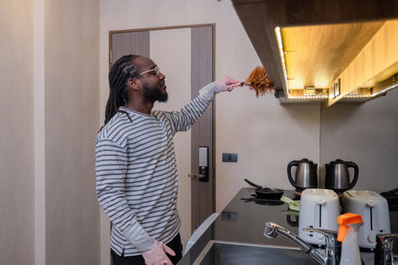 Happy young African American man dressed at home, doing housework, mopping the floor, cleaning the...