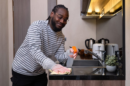 Happy young African American man dressed at home, doing housework, mopping the floor, cleaning the...