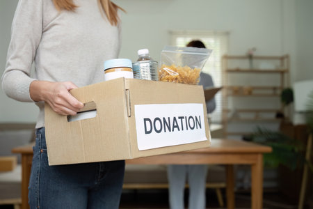 Beautiful female volunteer holds a donation box with canned food in it.の写真素材