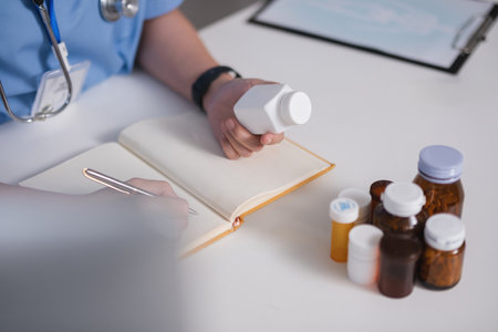 A doctor is writing in a notebook while holding a bottle of pillsの写真素材