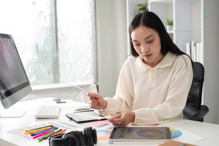 Female designer working in graphic design Choose colors for graphic design work. Focused work on a table full of colored paper for working on a computerの写真素材