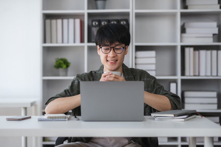 Young Asian student boy in private clothes studying online with laptop at home.の写真素材