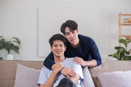 Happy Asian homosexual couple embrace on sofa in living roomの写真素材