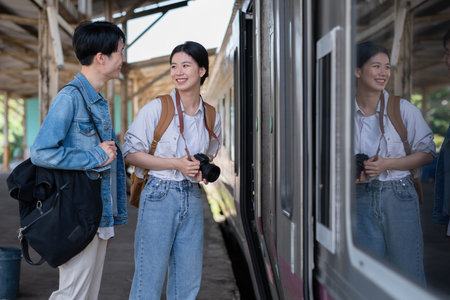 Happy young Asian couple carrying backpacks and cameras preparing to wait for the train at the train...