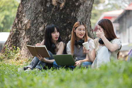 Happy Asian teenage female college students tutor together in the garden outside the university classroom. Female students happily help each other with their homework.の写真素材