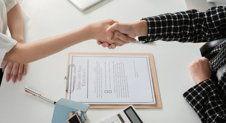 Real estate agent and client successfully discuss home purchase contract and shake hands to...