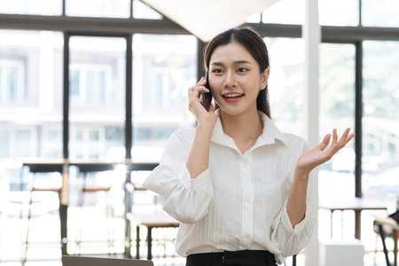 Beautiful Young Accountant Working in Modern Workspace, Professional Businesswoman Using Laptop and Smartphone, Focused on Financial Tasks, Bright Office Environment, Productive Work Atmosphereの写真素材