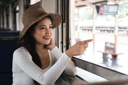 Asian woman pointing out train window with excitement, concept of explorationの写真素材
