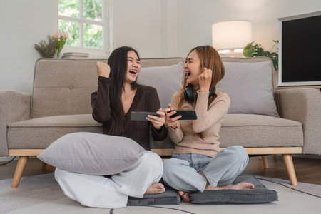 Lesbian and LGBT Couple Enjoying Fun Moments Playing Mobile Games Together in a Cozy Modern Living Roomの写真素材