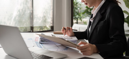 Young Female Accountant Working on Paperwork at Modern Office Desk with Laptop and Documentsの写真素材
