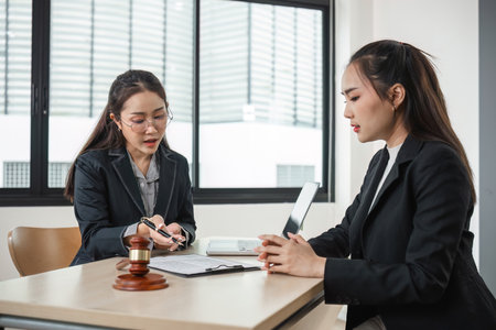 Young Lawyer Advising a Young Woman in a Modern Office Setting with Legal Documents and Gavel on Deskの写真素材