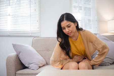 Young Woman Experiencing Menstrual Cramps While Sitting on a Couch in a Cozy Living Room Setting