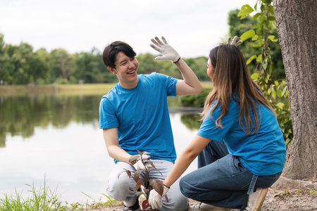 Happy Volunteer Couple Planting Trees Together by a Lake in a Park on a Sunny Day