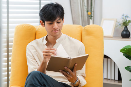 Young Man Relaxing in a Cozy Chair While Reading a Book in a Bright and Modern Living Room