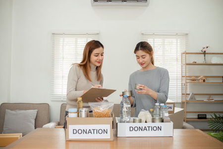 LGBT Lesbian Couple Preparing Items for Donation at Home, Sorting and Packing Clothes and Household Goods for Charityの写真素材