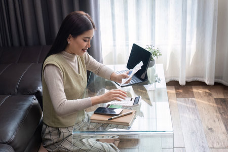 Young Woman Working from Home with Laptop and Documents in Modern Living Roomの写真素材