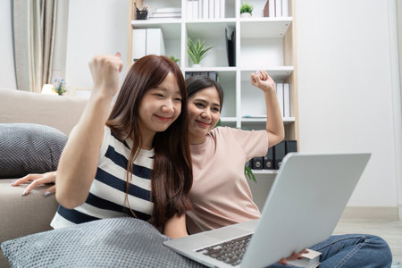 Young Women Celebrating Success in Online Studies at Home with Laptop, Happy and Excitedの写真素材
