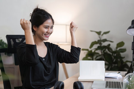 Successful Young Female Accountant Working from Home Celebrating Achievement in Modern Home Office Environmentの写真素材