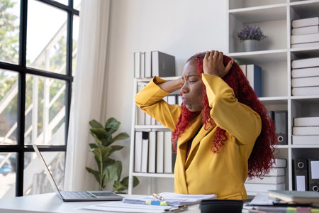 Stressed Young African American Business Woman Overwhelmed with Paperwork in Modern Office Settingの写真素材