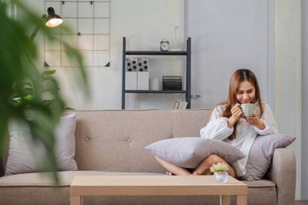 Young Woman Relaxing on Sofa with Coffee in Modern Living Room on a Peaceful Morningの写真素材
