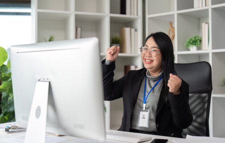 Successful Businesswoman Celebrating Achievement While Working on Computer in Modern Office Environmentの写真素材