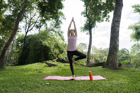 Young Woman Practicing Yoga in a Serene Park Setting Surrounded by Lush Greenery and Trees