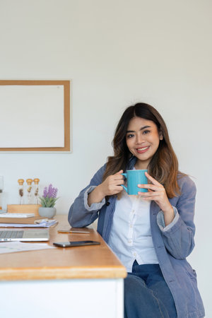 Young Woman Freelancer Working from Home with Laptop and Coffee in Modern Home Office Settingの写真素材