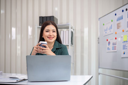 Young Accountant Working on Financial Document with Laptop and Coffee in Modern Office Settingの写真素材