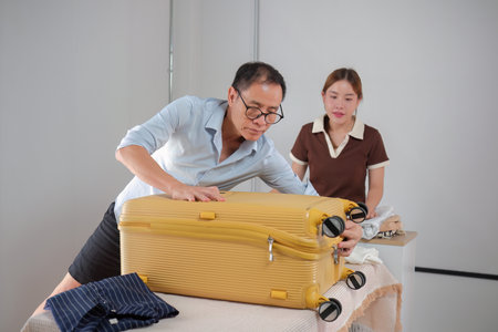 Father and Daughter Folding Clothes and Packing a Suitcase Together in a Modern Home Settingの写真素材