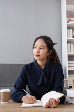 Focused Girl Studying Online with Notebook and Coffee in Modern Home Settingの写真素材