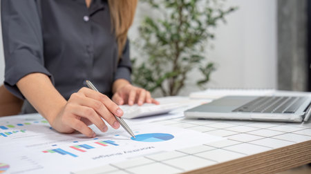 Young Female Accountant Analyzing Financial Data and Charts at Modern Office Desk with Laptop and...