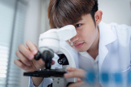 Young Researcher in Laboratory Examining Medicine Under Microscope for Scientific Study and Medical...