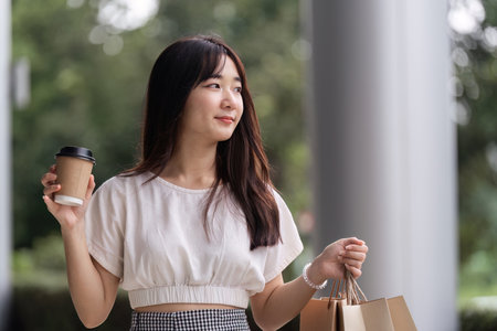 Young Woman Enjoying a Day at the Mall with Shopping Bags and Coffee in Hand, Embracing Modern Retail Experience and Fashion Trendsの写真素材