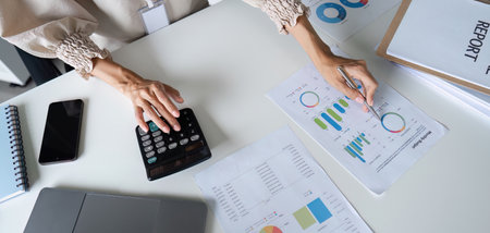Businessman Analyzing Financial Data with Calculator and Charts in Modern Office Settingの写真素材