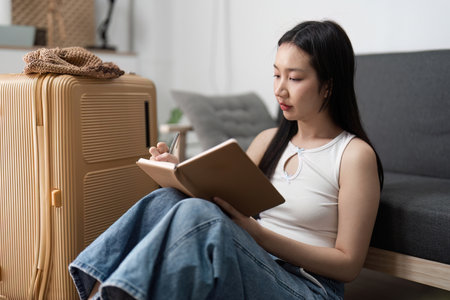 Young Woman Preparing for Travel by Packing Suitcase and Making Notes at Homeの写真素材