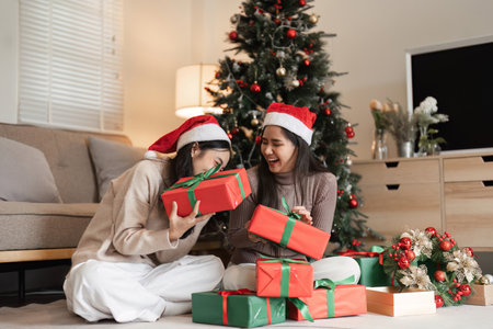 Joyful Young Couple Celebrating Christmas with Surprise Gifts in Cozy Living Room by Decorated Treeの写真素材