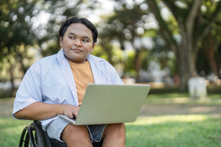 Young Man in Wheelchair Working Outdoors with Laptop in a Peaceful Garden Setting