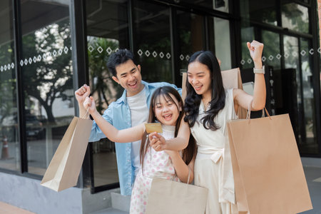 Happy Family Enjoying a Day of Shopping Together with Parents and Children Smiling and Holding Shopping Bags in a Modern Urban Settingの写真素材