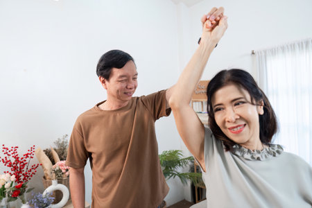 Joyful Retired Couple Dancing Together in Their Cozy Living Room, Embracing Life and Happiness in a Warm and Inviting Home Settingの写真素材