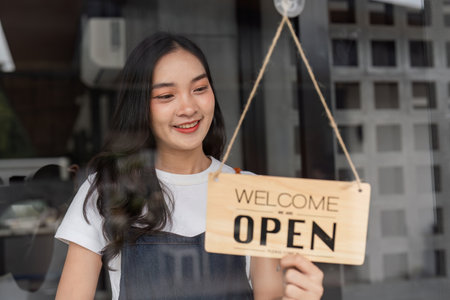 Cafe Staff Preparing for Opening with Smiling Barista Hanging Open Sign on Glass Door in Modern...