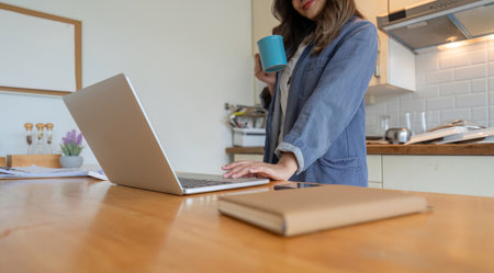 Woman Working from Home in Dining Room with Laptop and Coffee Cup in Modern Kitchen Settingの写真素材